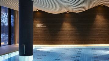 Una piscina interior moderna con pared de ladrillo oscuro y techo de diseño ondulado.