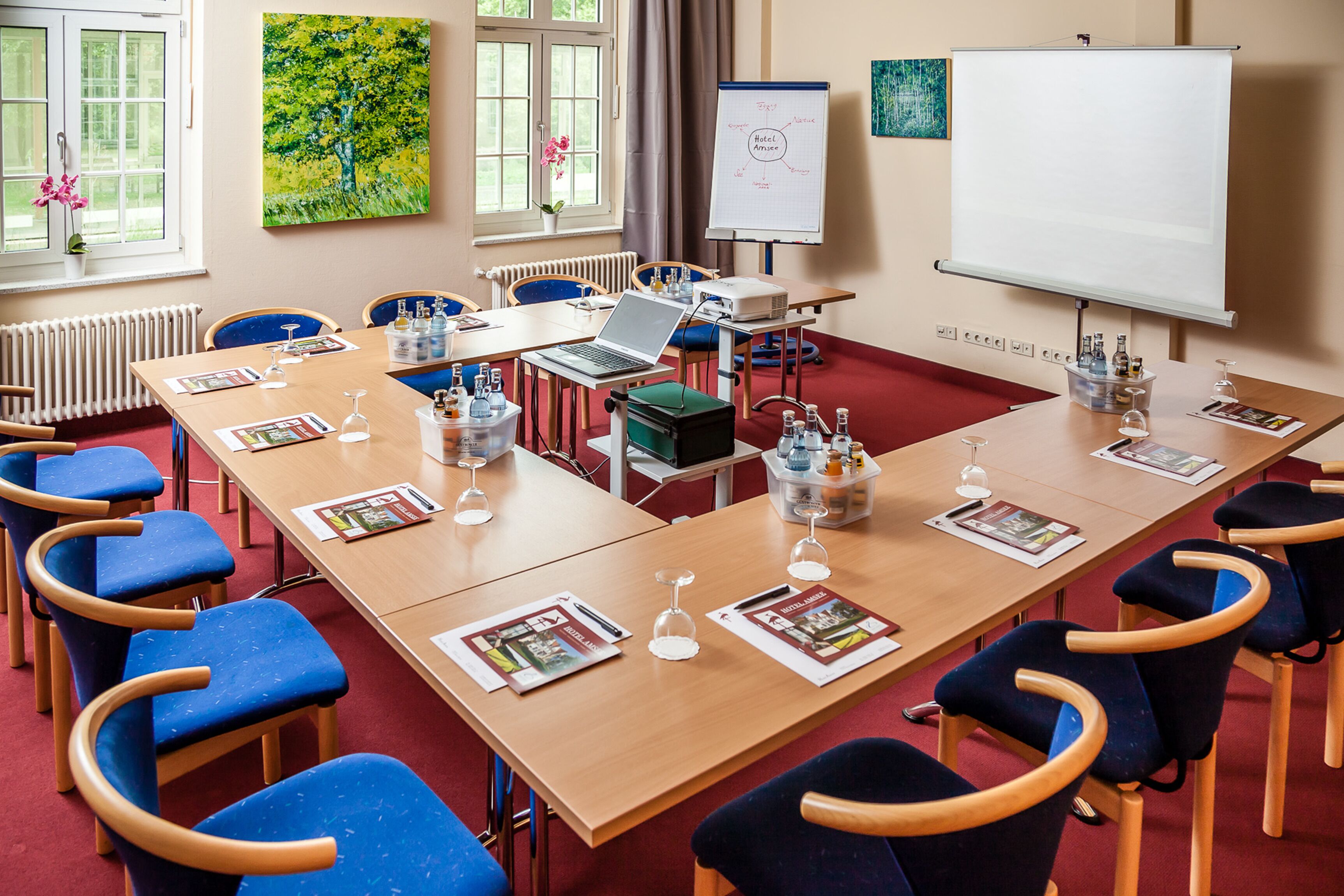 Ein Konferenzraum mit langem Tisch, blauen Stühlen, einer Whiteboard-Tafel und einem Projektor.