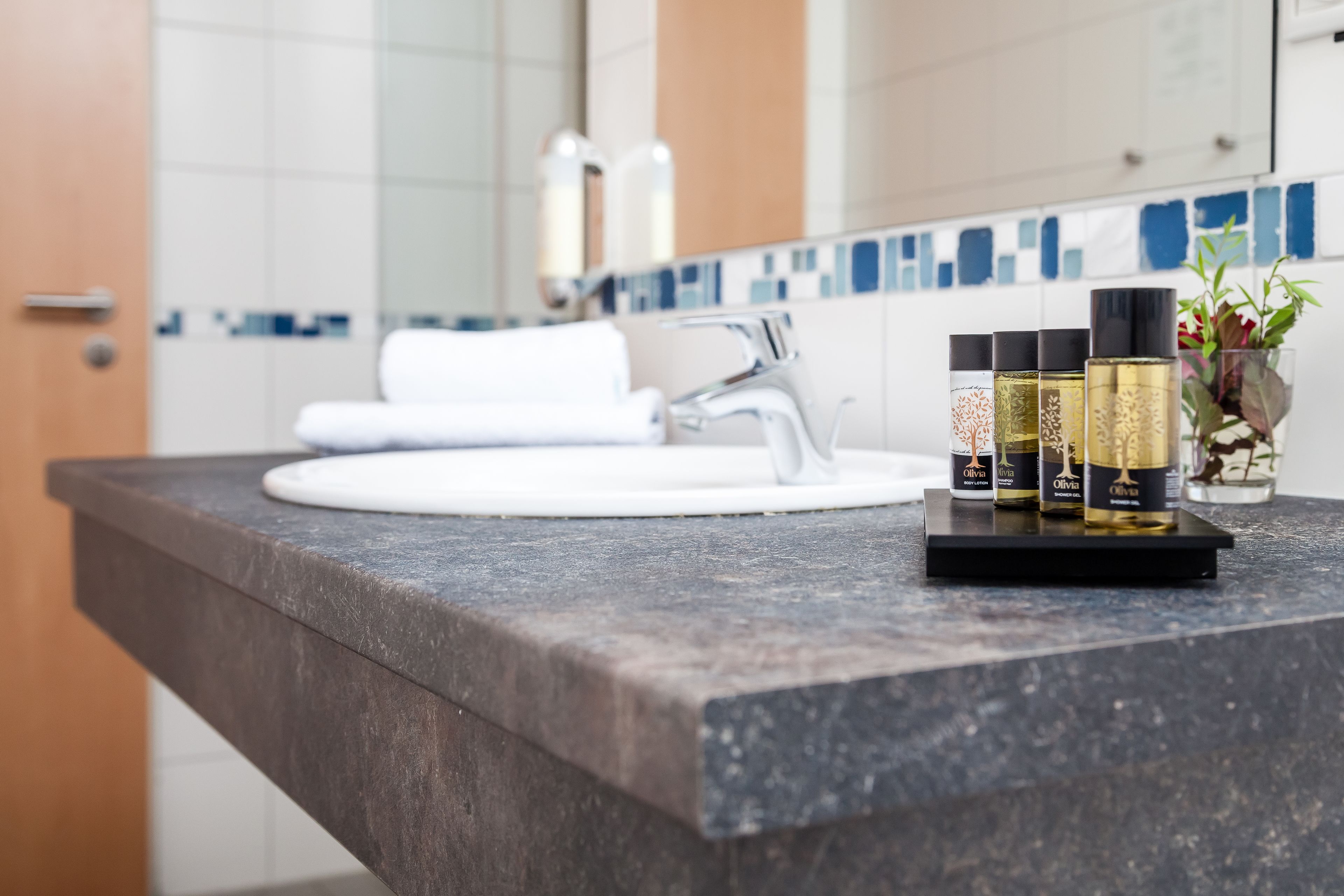 A bathroom with a marble countertop, a white sink, and a mirror. There are four bottles of olive oil on the counter.