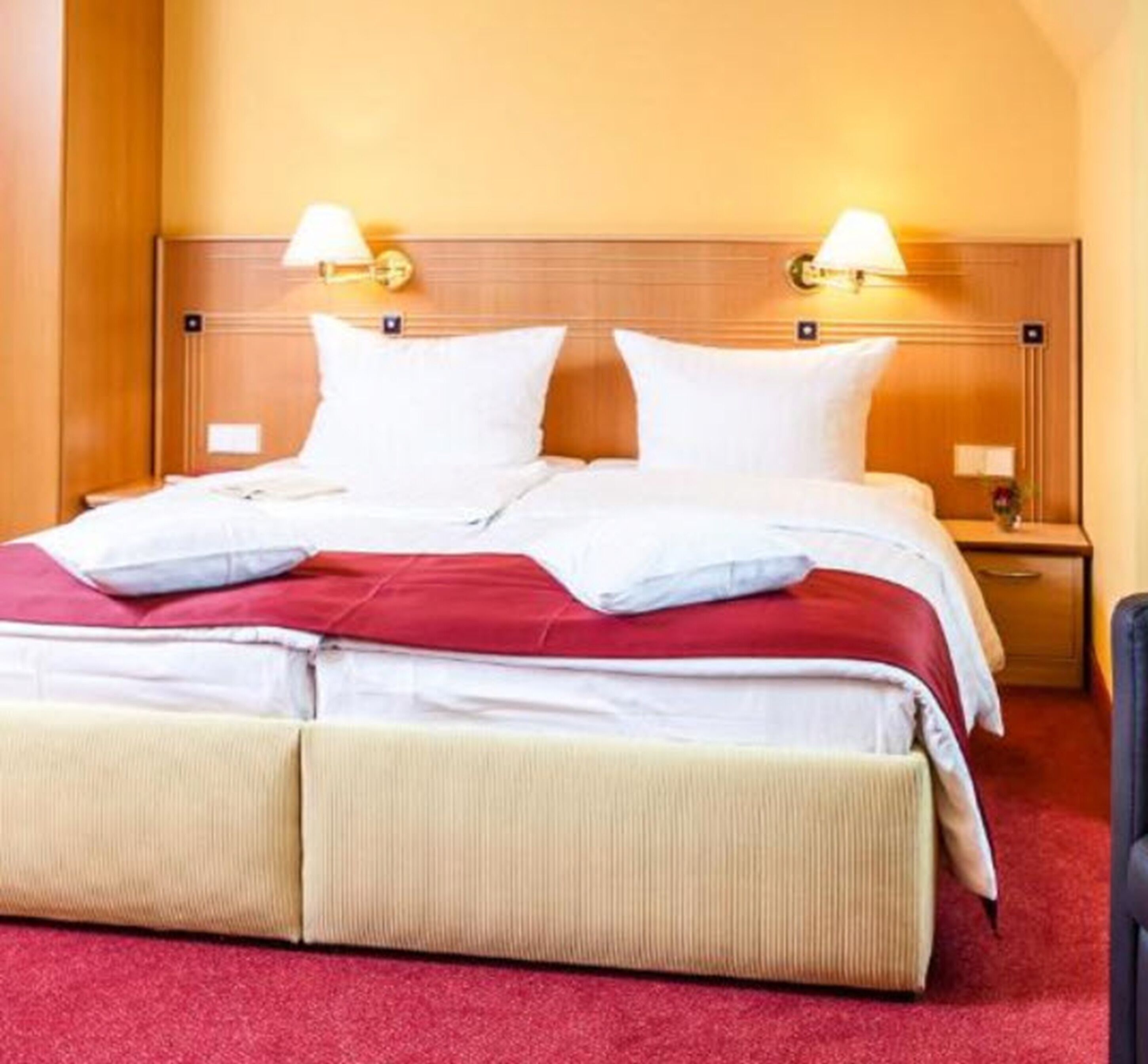 A hotel room with a large bed, two bedside lamps, a wooden headboard, and a red carpet.