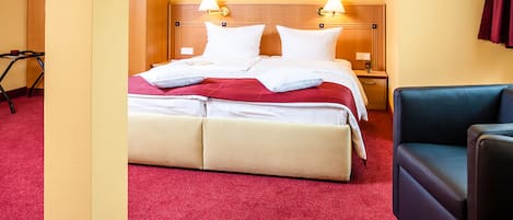 Une chambre d’hôtel avec un lit, deux lampes de chevet, une table de nuit, un fauteuil bleu et une moquette rouge.