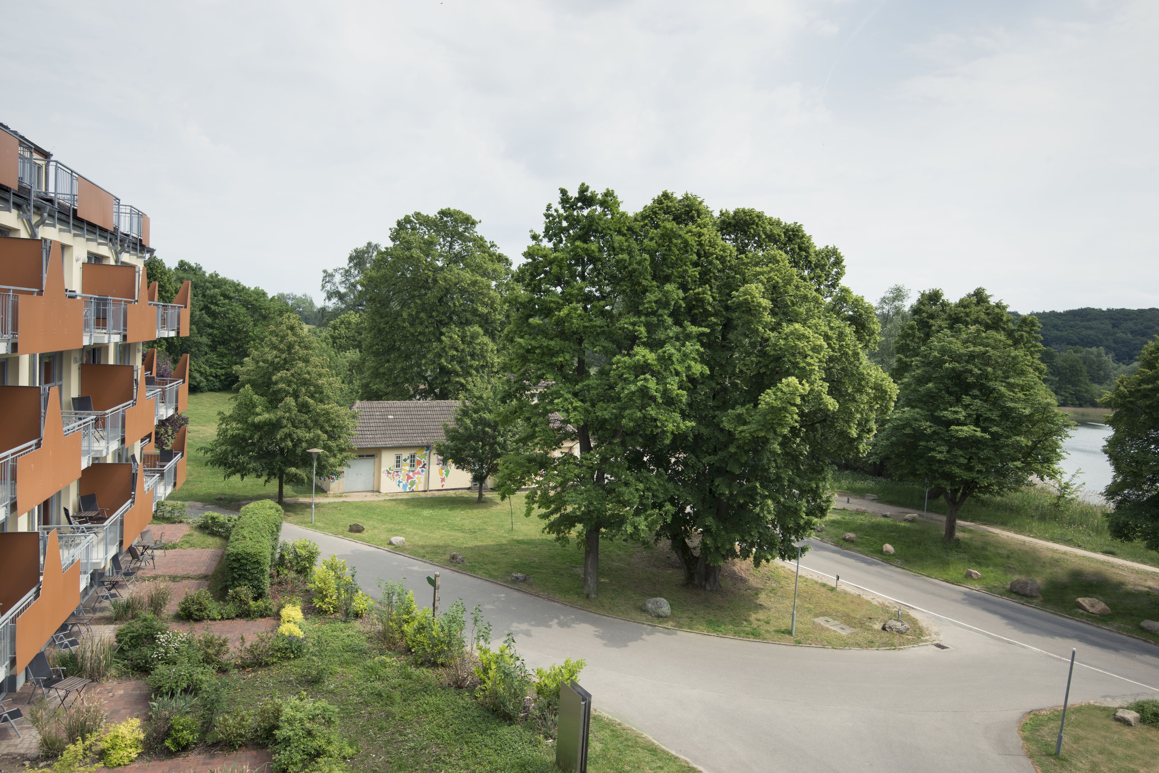 Ein mehrstöckiges Gebäude mit Balkonen, ein kleiner Garten mit einem Pfad und Blick auf einen See.