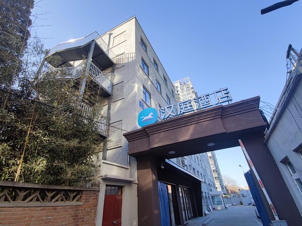 A hotel entrance with a sign, a gated driveway, and a building with multiple floors and balconies. - Hanting Hotel (Beijing)