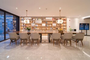 Une bibliothèque moderne avec une longue table et des chaises, entourée d’étagères, et une grande fenêtre sur un des murs.