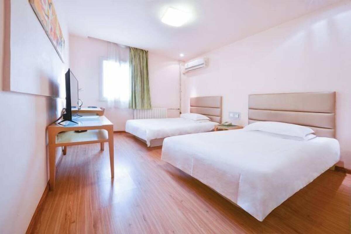 Una habitación de hotel con dos camas, un escritorio, un televisor y aire acondicionado.