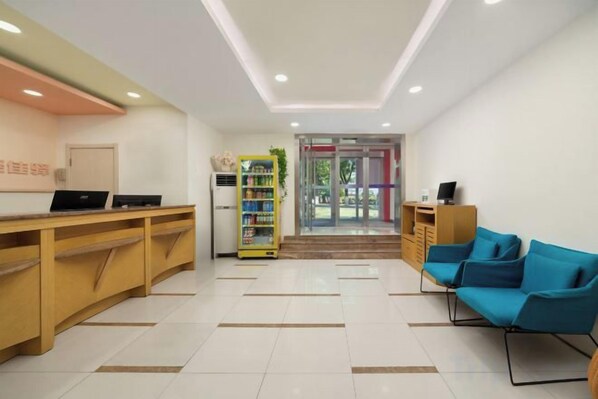 A reception area with a desk, a vending machine, and blue chairs.
