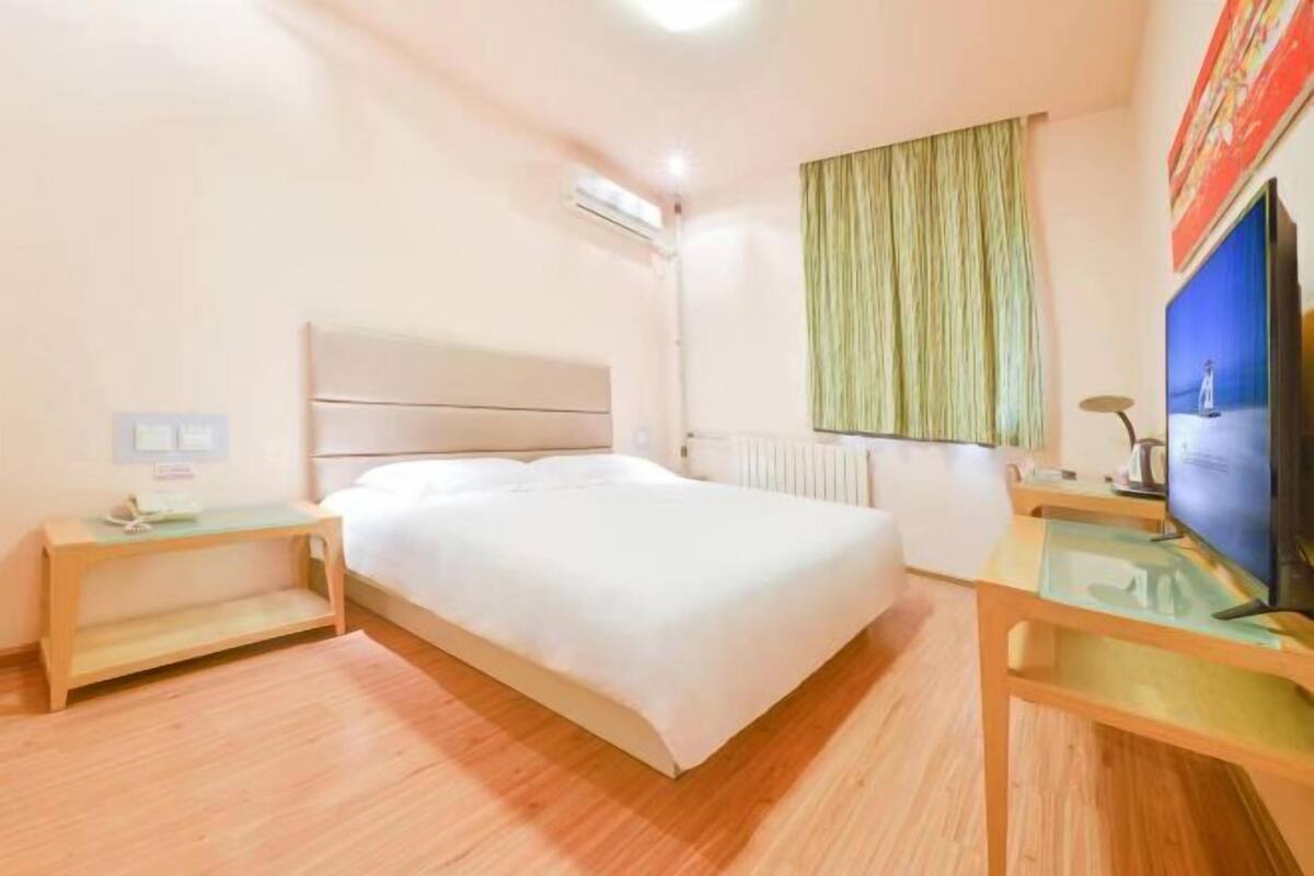 Una habitación de hotel con cama, mesitas de noche, televisor y ventana con cortinas.