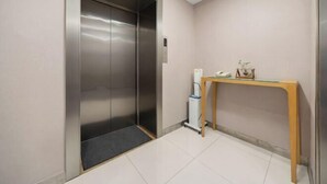 An elevator with a metallic finish, a small table with a telephone and decorative items, and a tiled floor. - Ginza Jiayi Hotel (Yantai Suocheng Wanda Plaza Branch) (Yantai)