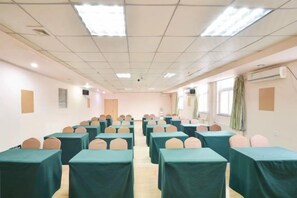 Un salón de conferencias con filas de mesas y sillas, equipado con luces en el techo y ventanas.