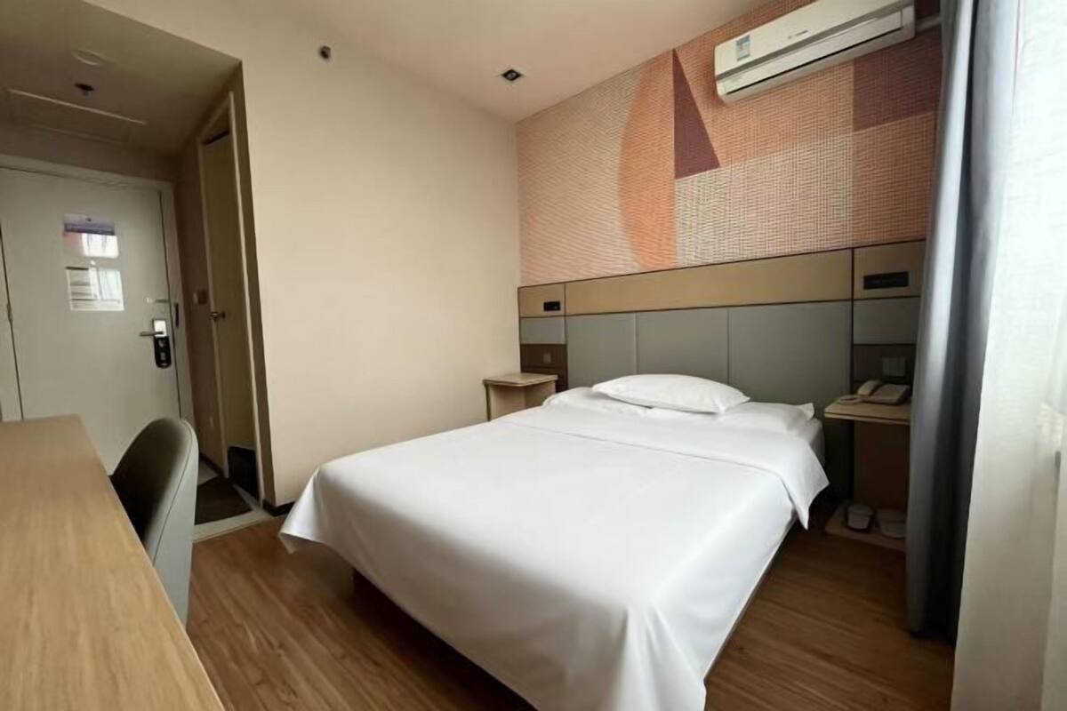 Habitación de hotel con cama, escritorio, silla, mesita de noche y aire acondicionado instalado en la pared.
