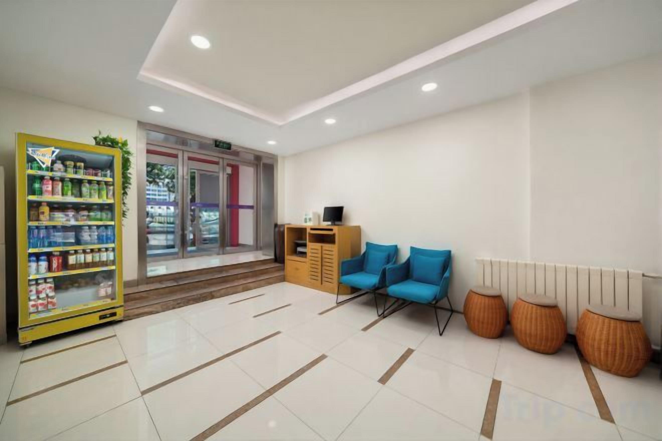 A reception area with a vending machine, a seating area with blue chairs, and a wooden cabinet.