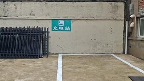 Suelo de concreto con una línea blanca marcada, una reja metálica y un letrero verde con caracteres chinos.