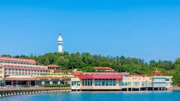 Un hotel costero con un faro al fondo, un muelle que se adentra en el agua y edificios con tejados rojos.