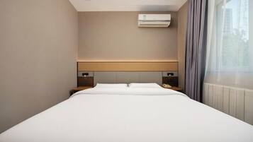 Habitació d'hotel amb un llit, taules de nit, un aire condicionat i una finestra amb cortines.