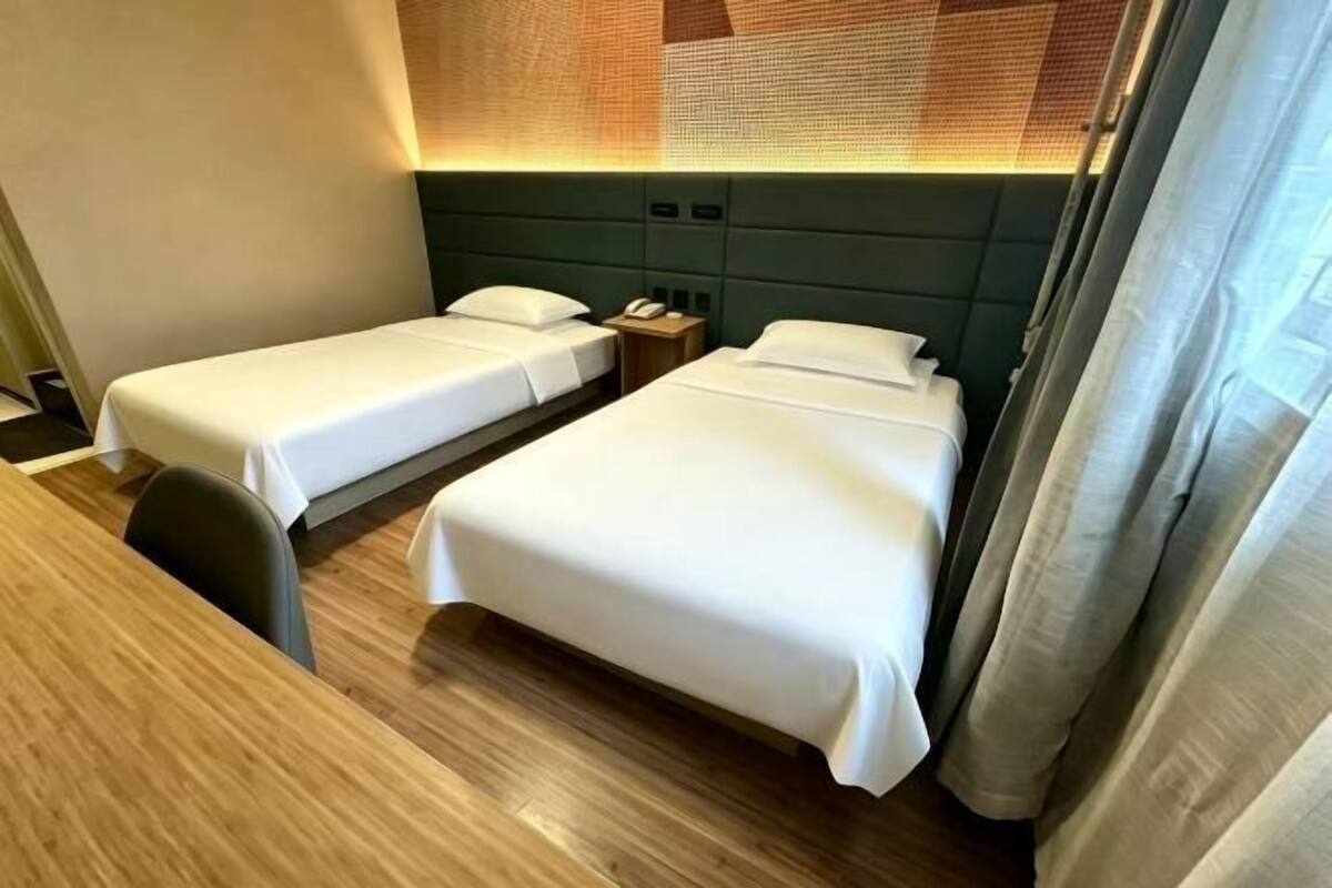 Habitación de hotel con dos camas, un escritorio de madera y cabecera con diseño texturizado.