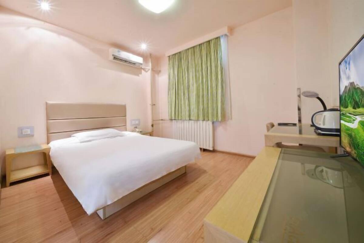 Habitación de hotel con cama, mesita de noche, televisión y ventana con cortinas.