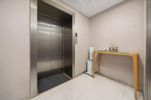 An elevator with a metallic finish, a small table with a telephone and decorative items, and a tiled floor. - Ginza Jiayi Hotel (Yantai Suocheng Wanda Plaza Branch) (Yantai)
