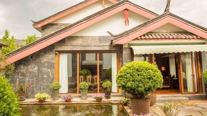 Un bâtiment traditionnel avec une façade en pierre, de grandes fenêtres et un petit étang agrémenté de plantes en pot.