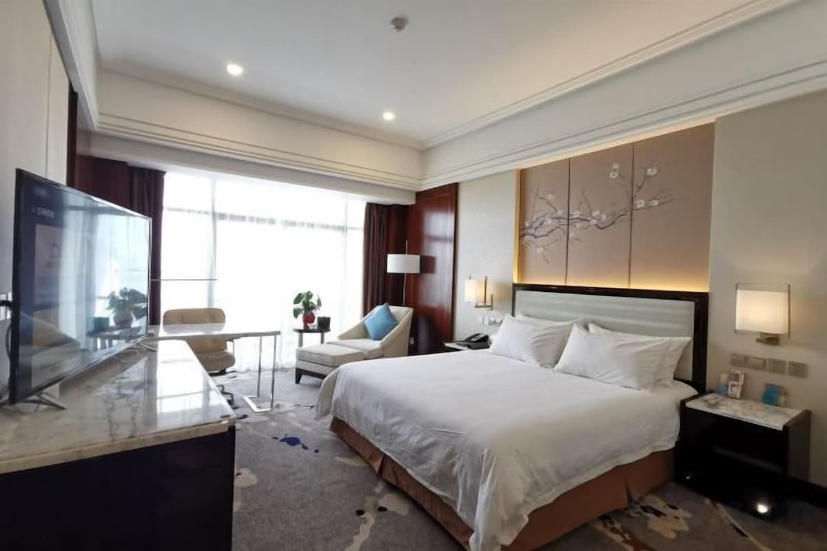 A hotel room with a bed, a desk, a chair, a television, and a window.
