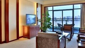 A modern living room with a television, a coffee table, and a sofa. There is a large window providing a view of the cityscape. - Mengjiang Hotel (Wenzhou)