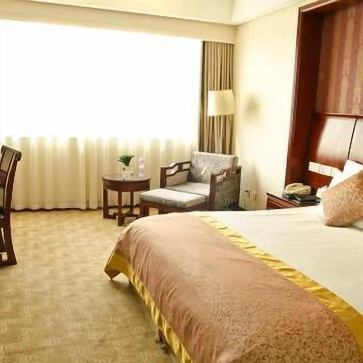A hotel room with a bed, a chair, a small table, and a lamp.