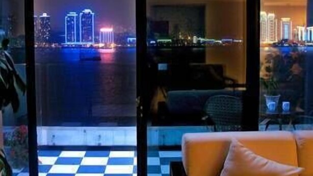 A room with a checkered floor, a sofa, and a view of a cityscape at night. - Mengjiang Hotel (Wenzhou)
