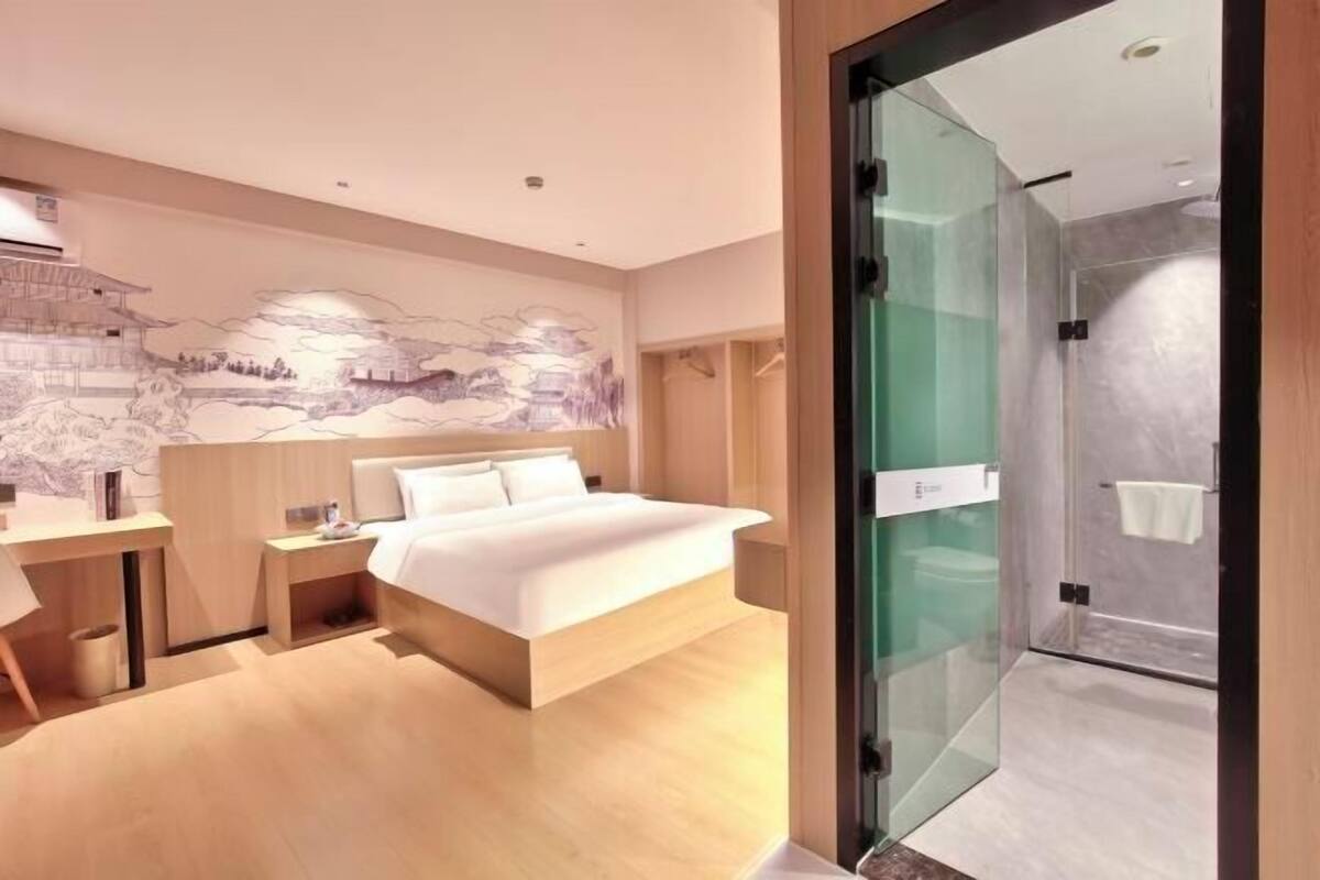Une chambre d’hôtel moderne équipée d’un lit, d’un bureau, d’une douche en verre et d’une fresque murale.