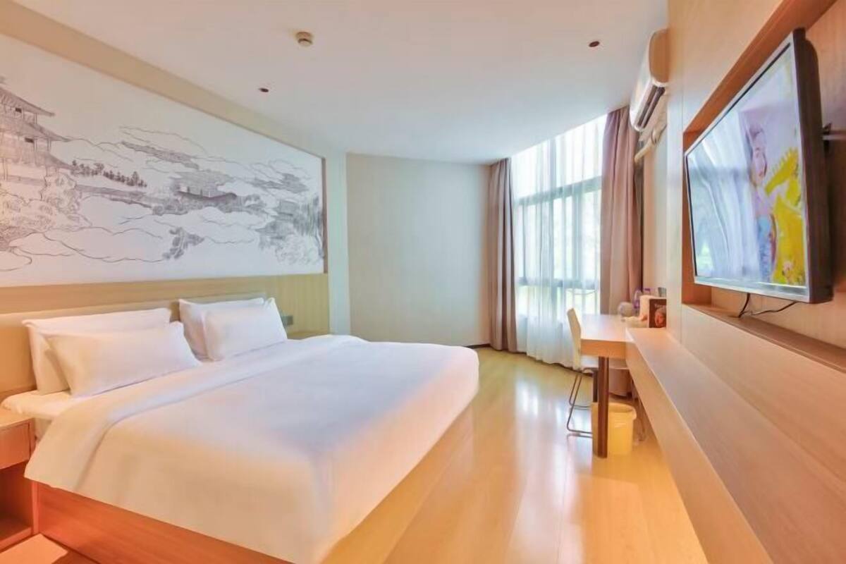 Une chambre d’hôtel avec un grand lit, un bureau, une télévision et une fresque murale.