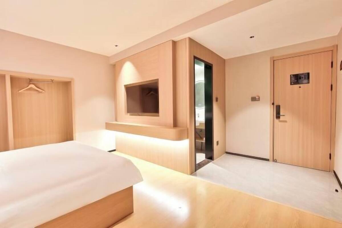 Une chambre d’hôtel avec un lit, une armoire, un miroir et une porte.