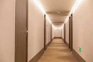 Un largo pasillo de hotel, estrecho, con puertas a ambos lados, pisos alfombrados e iluminación en el techo.