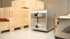 A stainless steel toaster with a wooden side table and a drawer unit.
