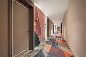 Un couloir d’hôtel avec des portes sur le côté gauche, une moquette à motifs et un mur uni sur le côté droit.