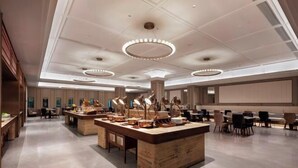 Un hall d’hôtel moderne doté d’un comptoir d’accueil central, de plusieurs espaces de détente et d’un grand écran pour les présentations.