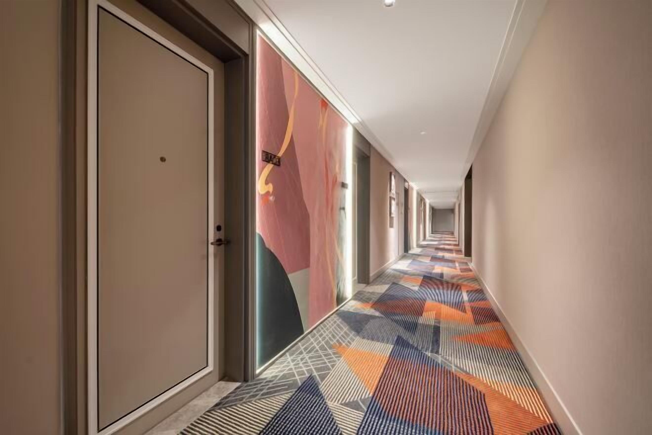 A hotel corridor with doors on the left, colorful patterned carpet, and plain walls.