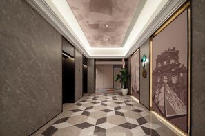 A hallway with a checkered floor, a large framed picture on the wall, and an elevator. - Fuyuan Hotel (Zhengzhou East Station Provincial Government Branch) (Zhengzhou)