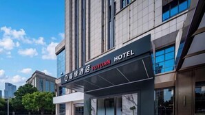 L’entrée d’un hôtel, avec une façade moderne, de grandes fenêtres et un ciel dégagé.