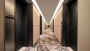 Un couloir d’hôtel avec un tapis à motifs, des portes des deux côtés et un panneau indiquant le numéro des chambres sur le mur de gauche.