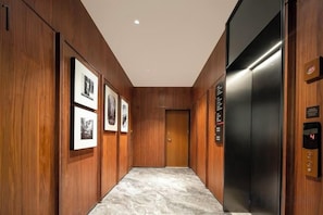 A hallway with wooden paneling, framed pictures on the wall, and a modern elevator. - Fuyuan Hotel (Zhengzhou East Station Provincial Government Branch) (Zhengzhou)