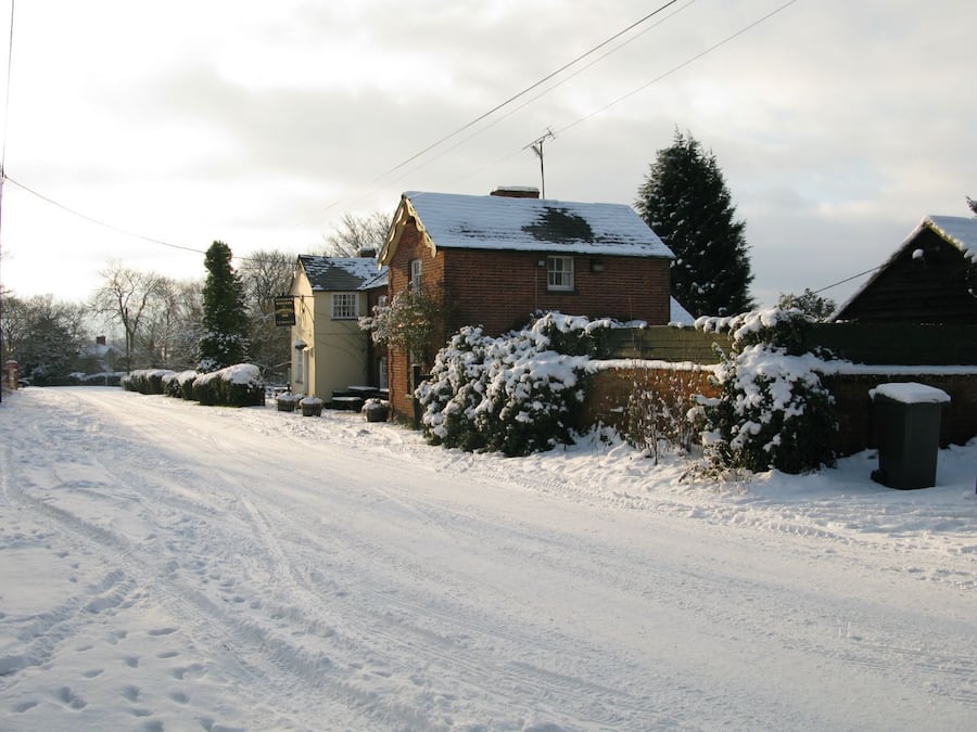 Une route de campagne enneigée, avec des maisons de chaque côté.
