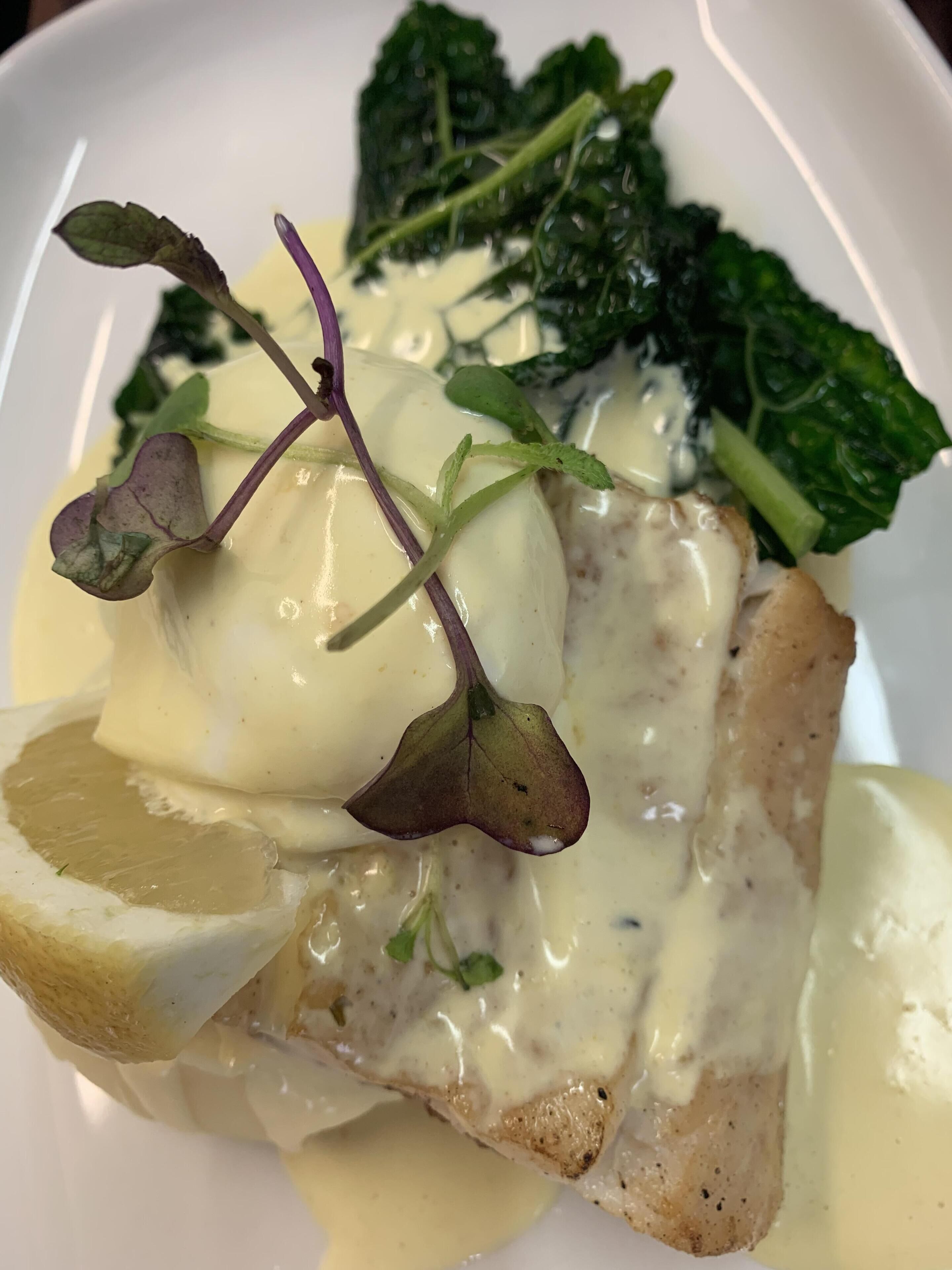 En tallrik med mat, bestående av en bit fisk täckt med hollandaisesås, serverad med grönsaker och en klyfta citron.