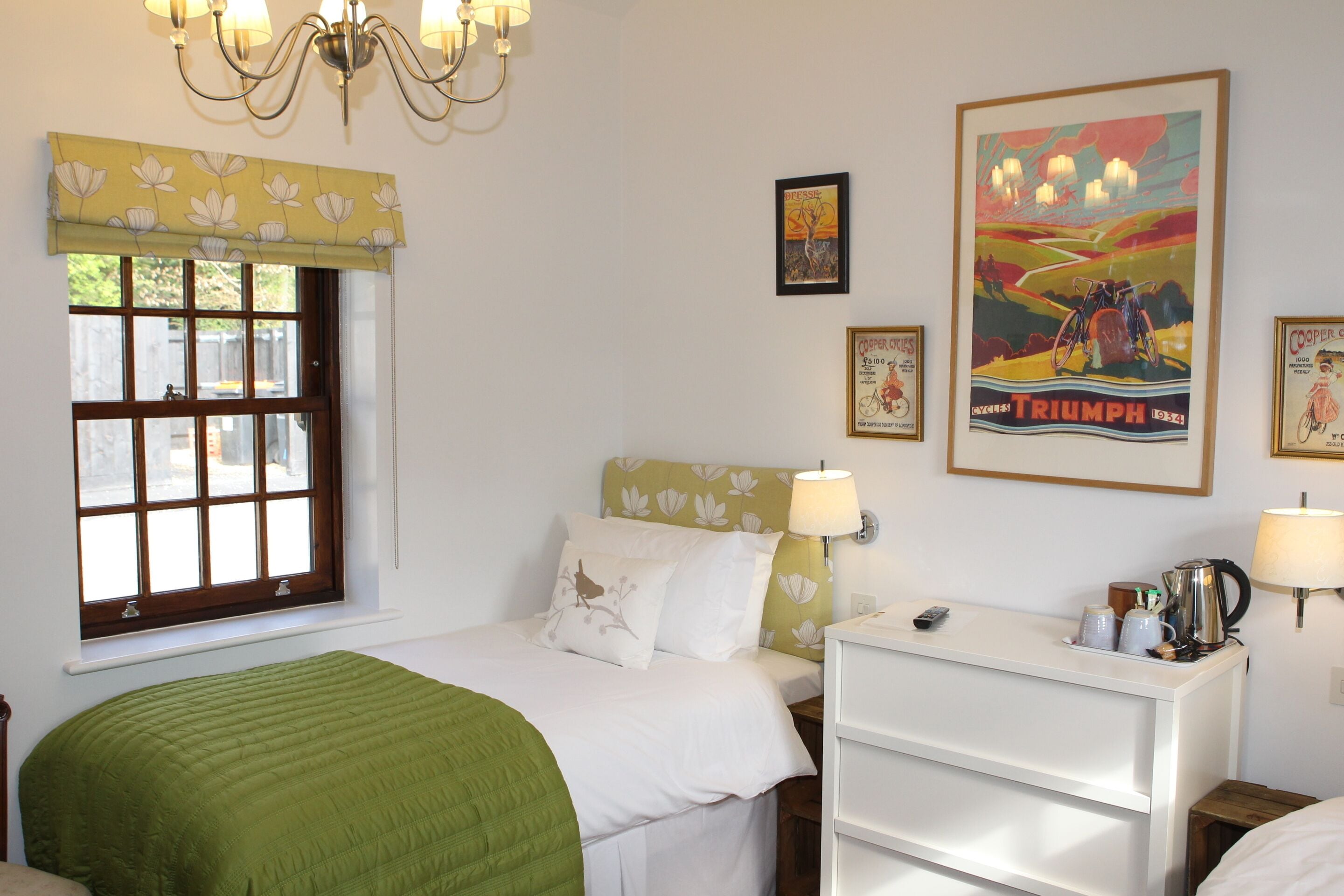 Quarto com cama, mesa de cabeceira, penteadeira, janela com vista e decoração nas paredes, incluindo um pôster da Triumph.