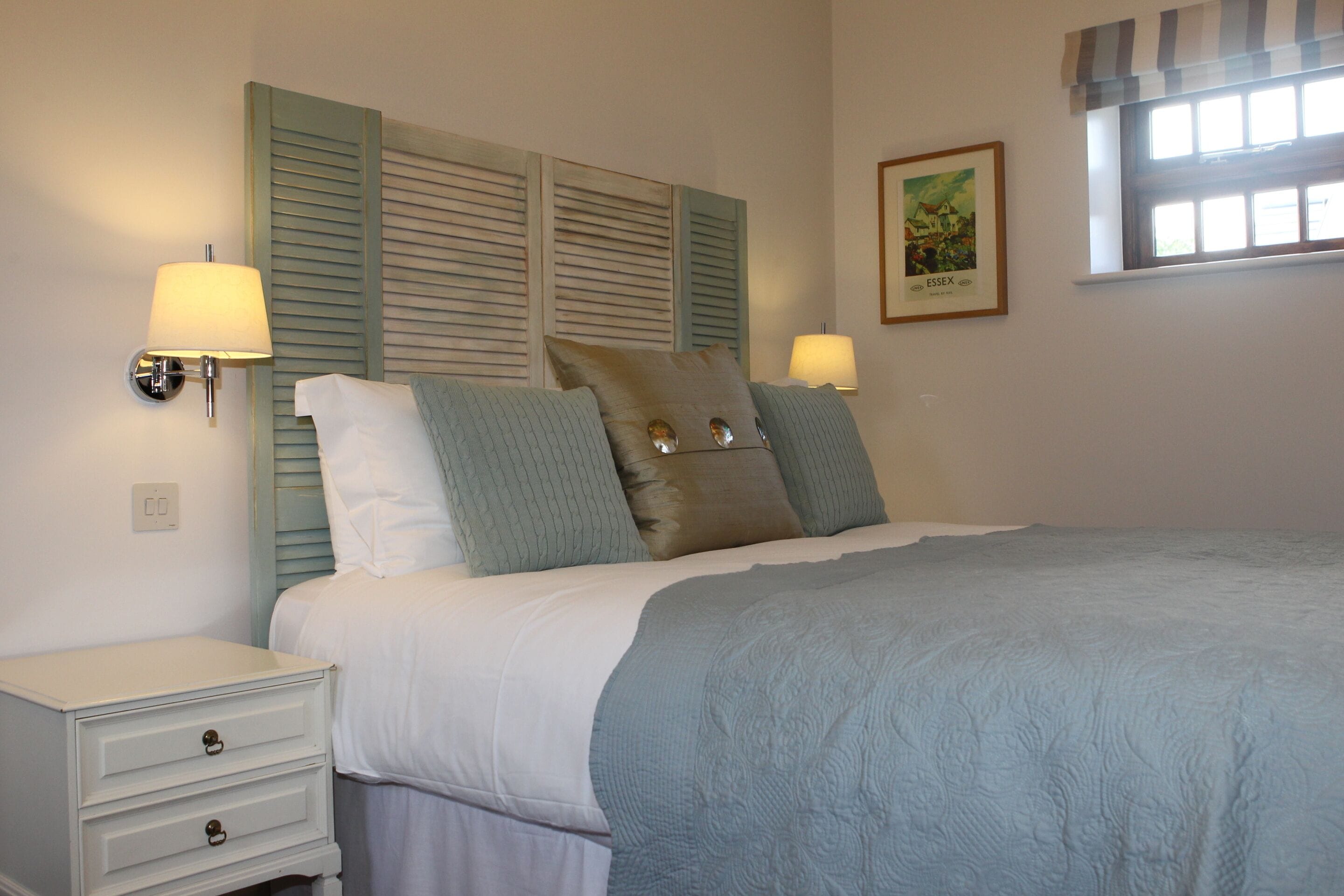 A bedroom with a bed, two bedside lamps, a nightstand, and a framed picture on the wall.