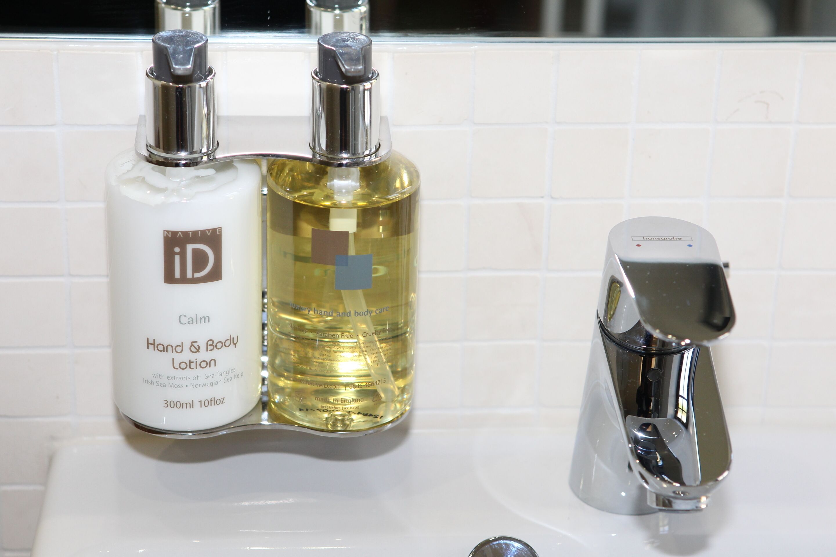 A bathroom sink with two bottles of hand and body lotion and a modern faucet.