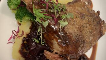 A plate with a roasted duck leg, broccoli, purple cabbage, and a dark sauce.