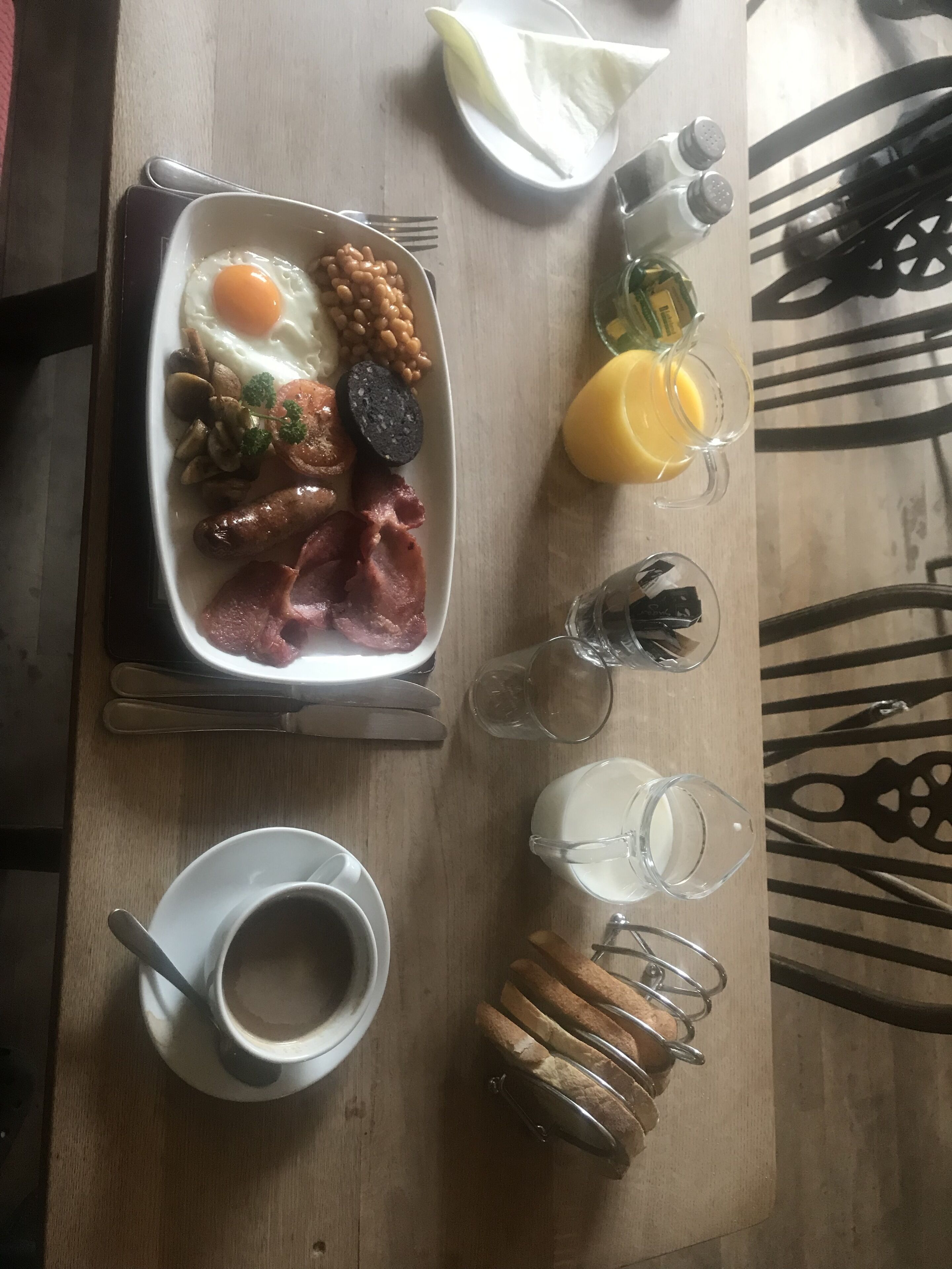 Un plato de desayuno con huevos, frijoles, champiñones, salchicha y jamón. Hay salsas, un vaso de jugo de naranja y una taza de café sobre la mesa.