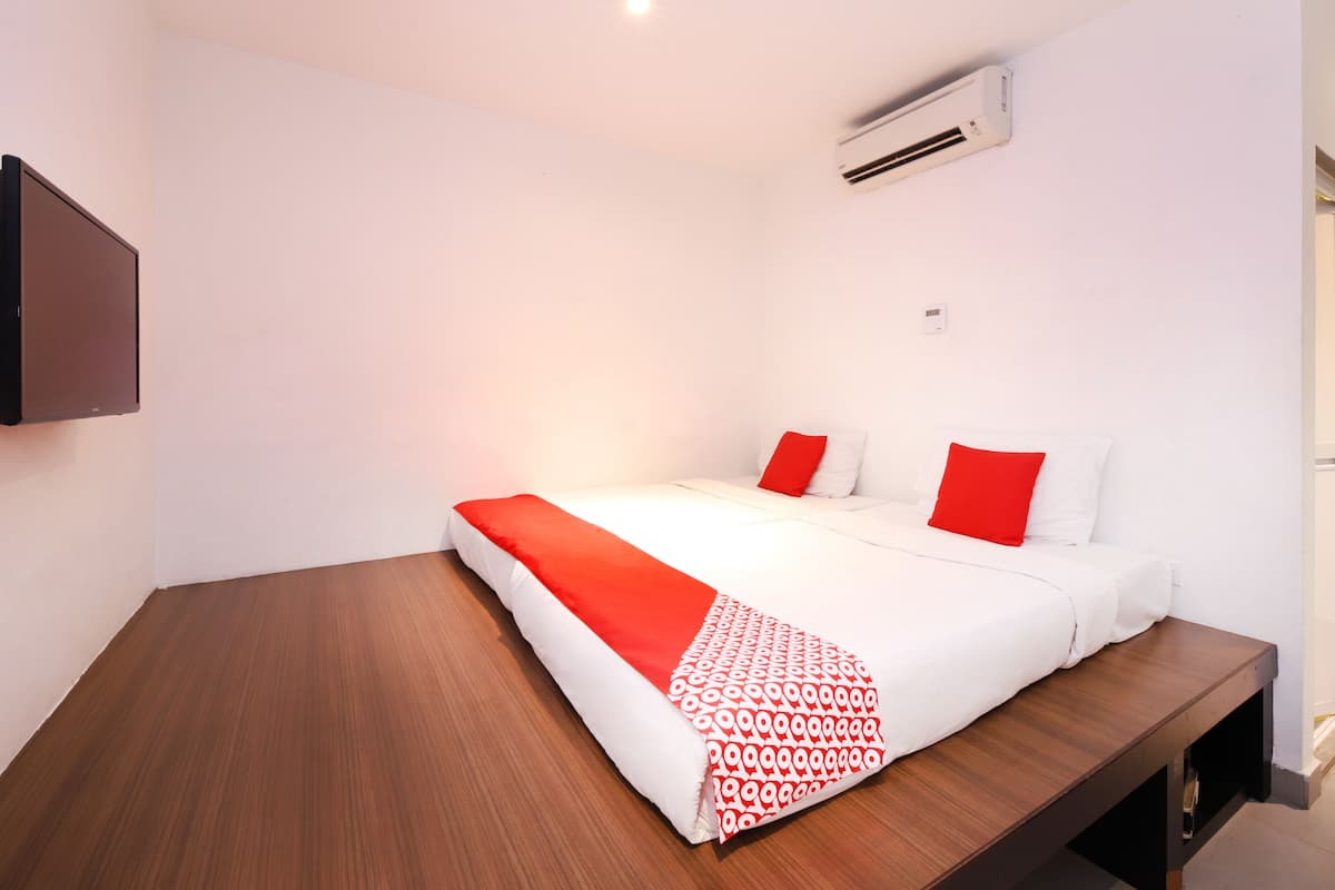 A modern hotel room with a wooden floor, a large bed with white and red bedding, a mounted TV, and a wall-mounted air conditioner.
