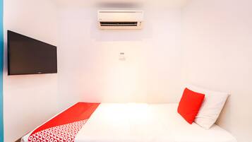 Una habitación pequeña y ordenada con una cama, un televisor de pantalla plana en la pared y un equipo de aire acondicionado sobre la cama.