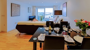 Een moderne woonkamer met een bank, een eettafel gedekt voor twee personen en een groot raam met uitzicht op de stad.