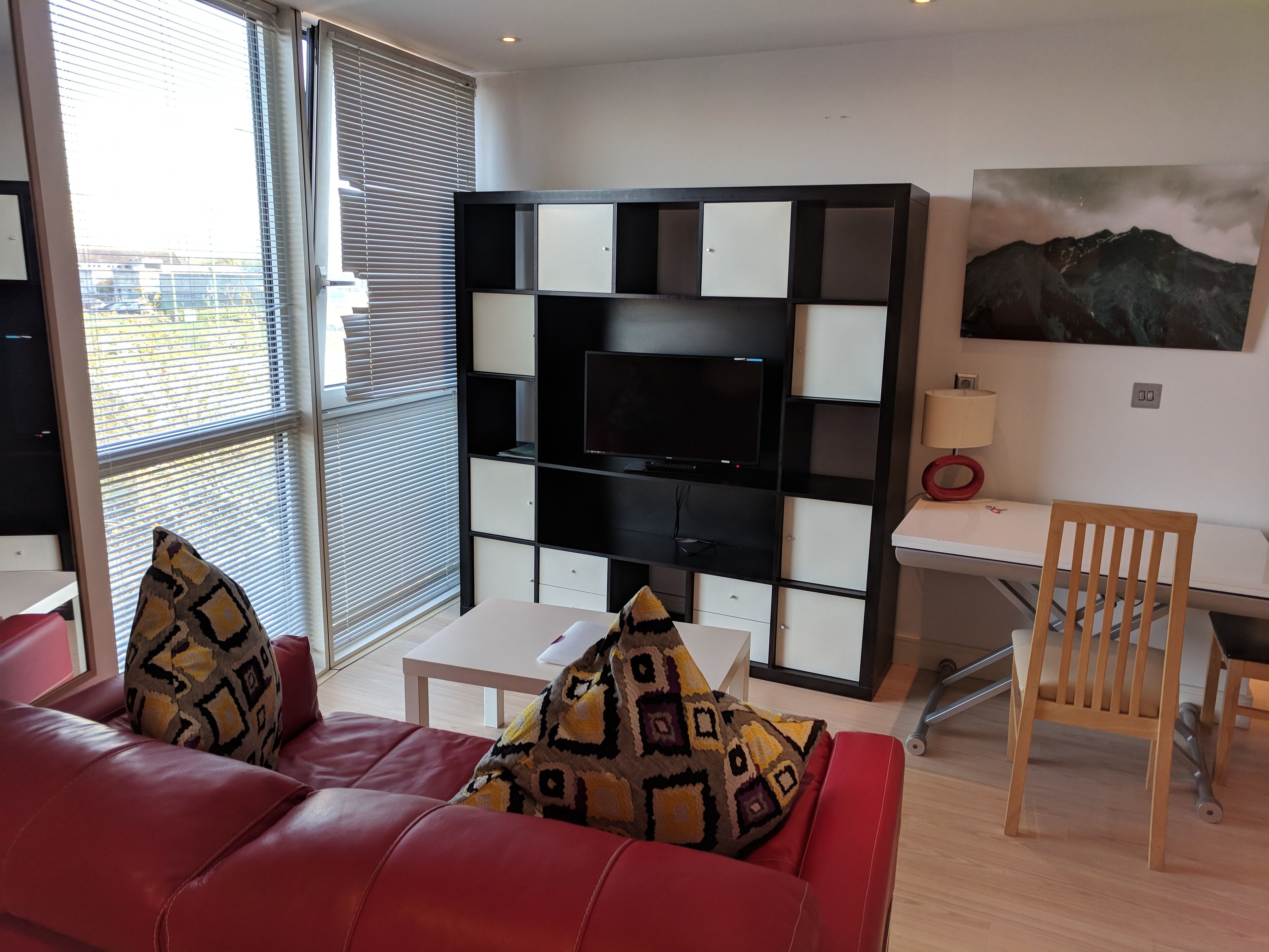 Ein modernes Wohnzimmer mit einem roten Sofa, gemusterten Kissen, einem weißen Couchtisch, einer schwarz-weißen Unterhaltungsanlage und einem Bild an der Wand.