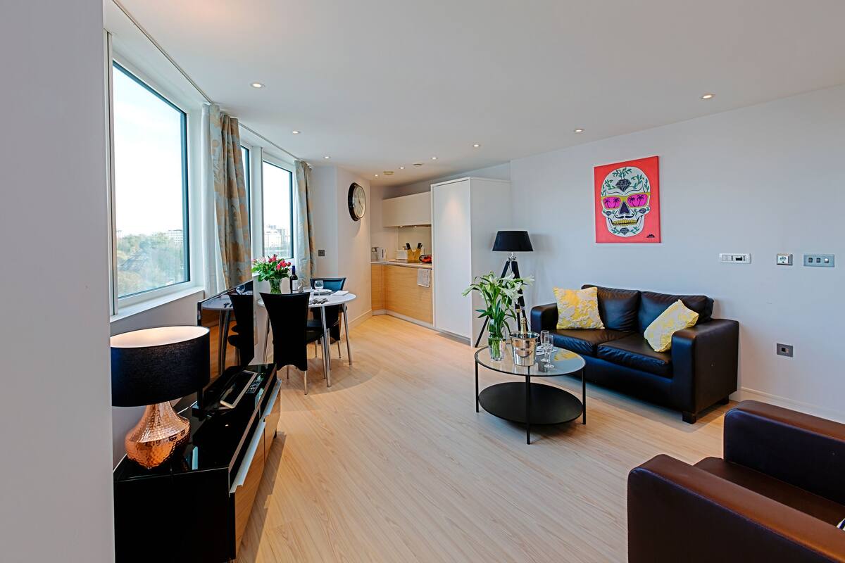 Un salon moderne avec un canapé, un coin repas comprenant une table et des chaises, et une cuisine en arrière-plan.